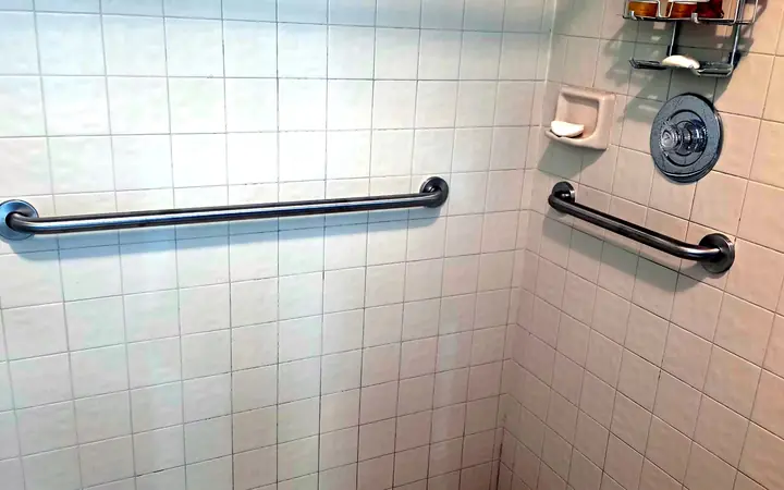 Horizontal and angled stainless grab bars installed on white tile in a shower, Longwood